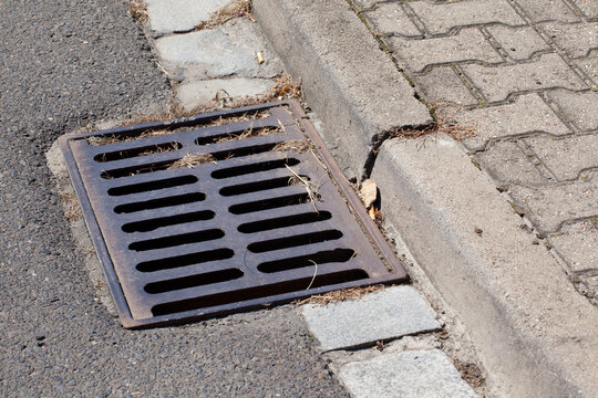 Steel sewer grate on the side of an asphalt road.