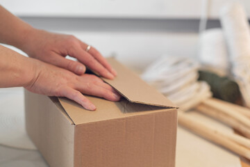 woman entrepreneur packs a handmade product in a cardboard box. delivery of goods for a small business. an elderly woman earns her hobby from home.