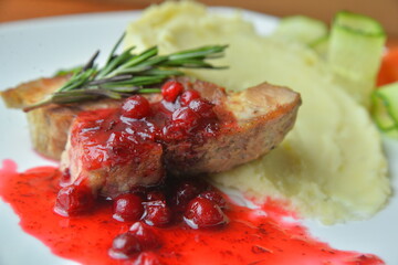 Roasted meat on white plate with mashed potato herbs and berry sauce