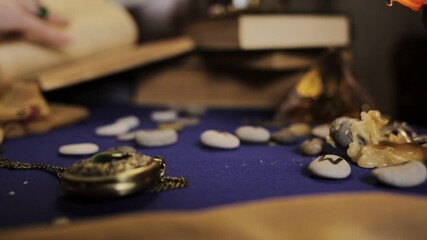 Astrology and esotericism. A woman fortune-teller reads runes and leafs through a book, a burning candle drips with wax next to it. Hands in rings and bracelets close-up. Side view. In the blur. - Powered by Adobe