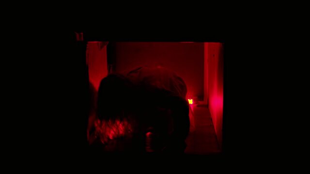 Scary woman in straitjacket crawling in ventilation shaft in red lighting - looking in the camera