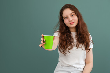 A girl shows a light green paper cup to the camera