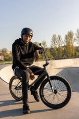 Fototapeta na wymiar Teenage boy wearing helmet sits on black bmx, low bike on ramp in spring, man doing sports, outdoor activity