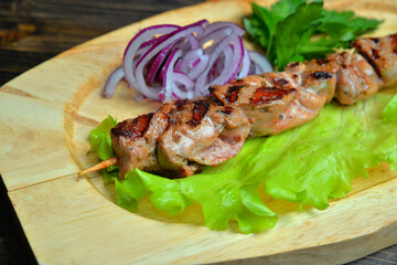 Grilled kebab meat on bamboo skewers on wooden plate