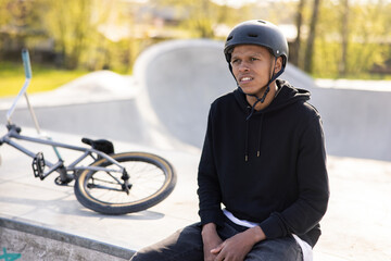 A young teenager sits on a concrete ramp with a bicycle knocked over next to him. The boy has a...