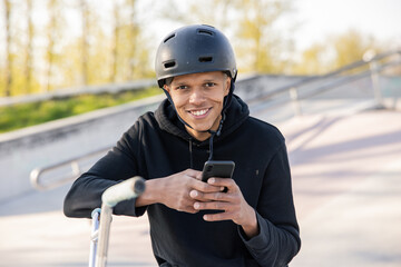 A teenager waits for classmates at the skatepark with his bike after school. Boy sits with helmet...