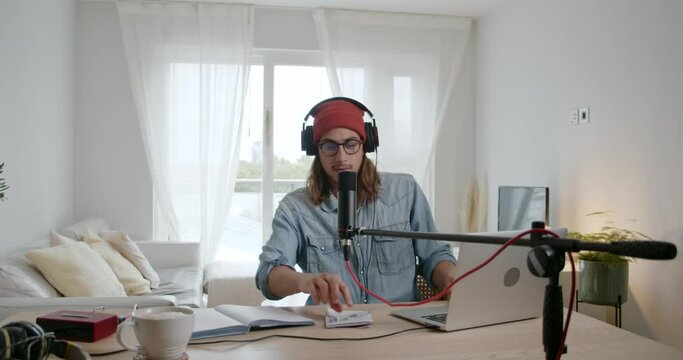 Caucasian male recording podcast in living room with relevant notes and technical equipment