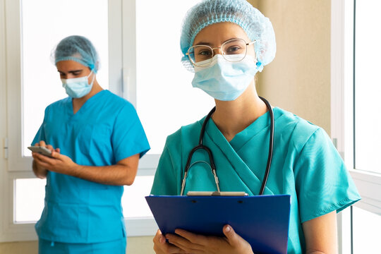 Doctor in uniform and with clipboard in clinic against blurred medic