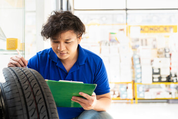 Asian male worker checking new tire wheel at wheel store. Salesman examining new tire at workshop....