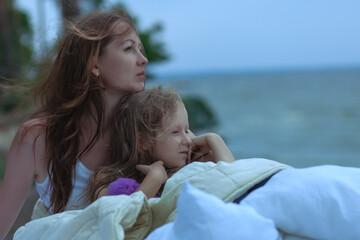 Woman with baby sleep on a bed outdoors by the ocean.