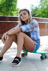 beautiful teenage girl with long hair in blue glasses and a plaid shirt on a skateboard