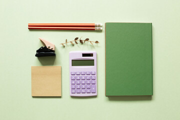 Notepad, stapler, pencil, calculator, notebook, eucalyptus leaf on green background. workspace. flat lay, top view - obrazy, fototapety, plakaty