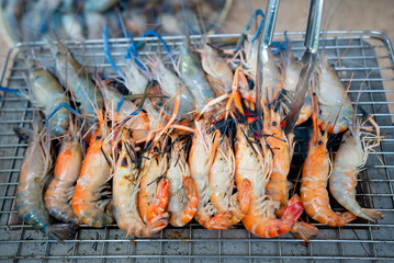A large number of shrimps were grilled on a charcoal grill, turning orange and almost ready to eat.