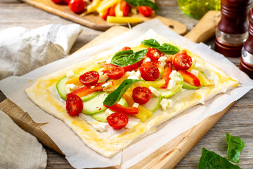 The process of making a puff pastry pie with a vegetable mixture and mozzarella cheese on a serving board on a culinary background closeup. Raw dough and baking ingredients on the table