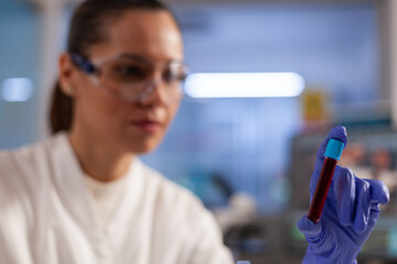 Chemical doctor holding blood flask for tests in scientific laboratory. Chemistry occupation woman with protection glasses and gloves working on treatment analysis and diagnose.