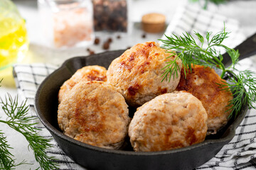 Turkey cutlets in a black frying pan on a light gray cooking table closeup	