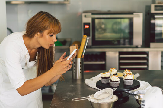 Confectioner girl photographing cupcake for her blog. Girl makes a photo of cupcakes on a smartphone