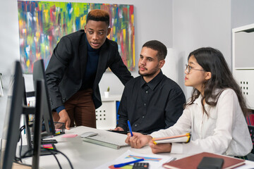 New employee is undergoing training in company experienced manager is explaining principles of computer programs to boy looking into monitor together next to him sits woman who is trainee's supervisor