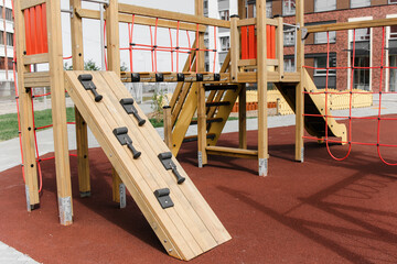 An outdoor colorful playground next to the house. A summer day. Children's playground with rubber floor covering. Close-up, details of a wooden house for children.