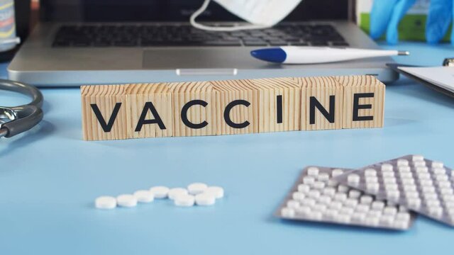 Vaccine is written on the wooden cubes that the doctor puts on the table. The appearing cubes with the word vaccine complement the medical table full of medicines