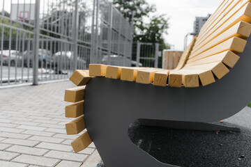 A new wooden bench with metal legs on the street. A summer day. Outdoor colorful playground with rubber flooring next to the house.