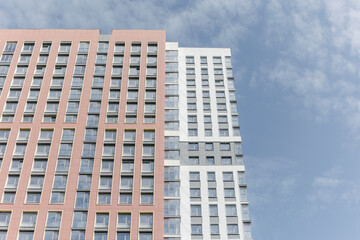 Obraz premium The facade of a high-rise residential building on a sunny summer day. a detailed picture of a building in the city. The blue sky is reflected in the windows.