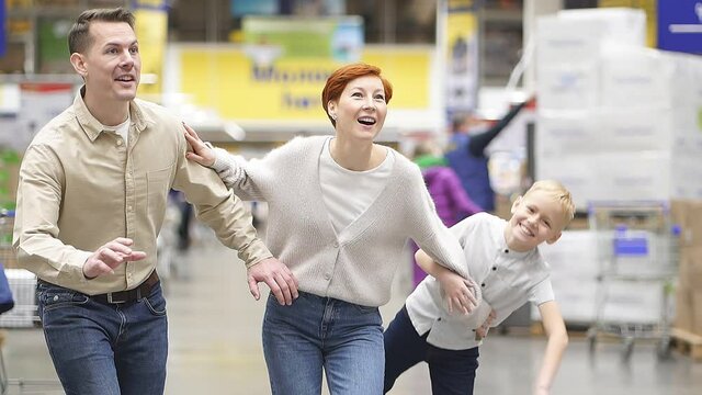 Family with child son run to discounted product, hurry up to make purchase. Caucasian parents and son in aisle of supermarket, cheerfully smiling, surprised and happy. Slow motion