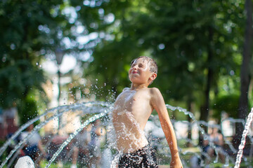 A little boy enjoys the cold waters of a fountain during the heat wave. Conceptual photography of hot weather, heat wave, global warming, summer season, climate change, enjoy life.