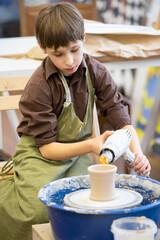 Fototapeta na wymiar A little boy makes a clay product at a potter's wheel.
