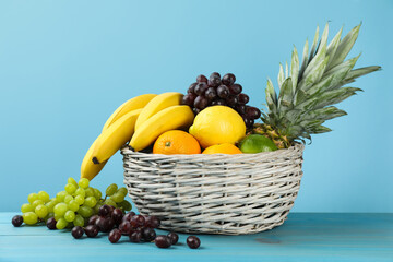 Wicker bowl with different ripe fruits on turquoise wooden table