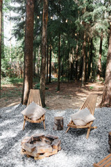 Wooden chairs around the fireplace. Pine forest. Family holidays in the country, fun trips in the fresh air. Rest on a picnic at a camping site.