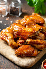 Homemade baked or fried chicken wings in barbecue sauce on a serving board on a cooking table closeup	