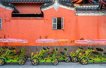 Some empty colorful rickshaws in front of red wall Chinese ancient buildings.
