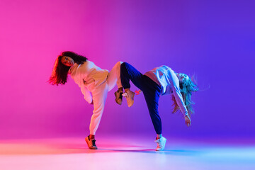 Two beautiful hip-hop girls dancing on gradient pink purple neon studio background