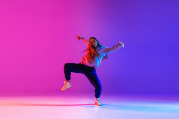 Attractive young girl dancing hip-hop isolated on gradient pink purple neon studio background