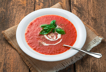 Tomato soup-puree with cream and fresh basil on a wooden background. Side view, close-up.