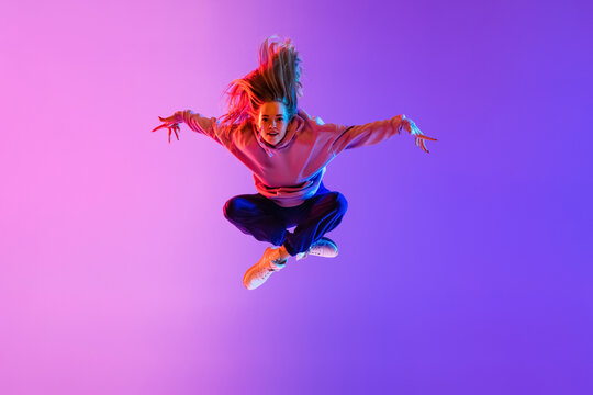 In jump. Young beautiful girl, female hip-hop dancer isolated on gradient pink purple neon studio background