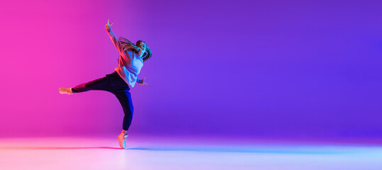 Attractive young girl dancing hip-hop isolated on gradient pink purple neon studio background