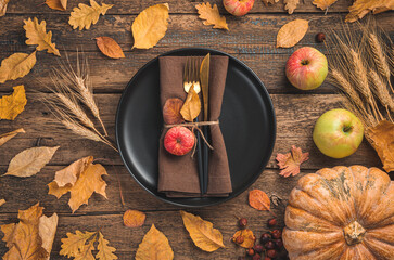 Festive, autumn background with a plate, serving napkin, cutlery, pumpkin and autumn leaves. The concept of Thanksgiving day.