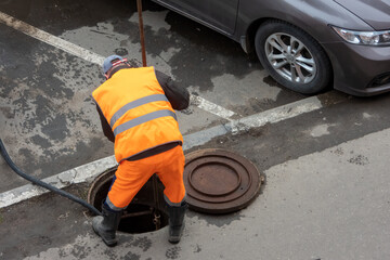 MOSCOW, RUSSIA - APR 25, 2020. Worker over the open sewer hatch - obrazy, fototapety, plakaty