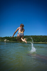 Fototapeta premium A little cute girl in a swimsuit jumps into the blue water of a career lake.