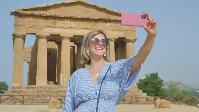 tourist woman taking a selfie in front of valley of the temples sicily,female visitor photograph herself with the temple of concordia in the background,agrigento italy