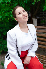 sexy confident brunette woman in red and white outdoors sitting on bench