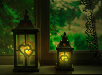 Stojące na parapecie okiennym w mieszkaniu lampiony z płonącymi wewnątrz nich świecami.