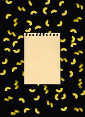 Italian pasta - Cornetti on a black background with a sheet of craft paper torn from a notebook. Creative culinary background for restaurant, menu, poster, advertisement.