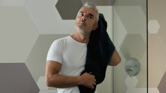 mature man after shower wipes his hair with a towel in front of the mirrow in the morning,adult mature caucasian male gets ready for the day