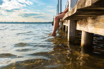 Female feet in the water near the wooden pier