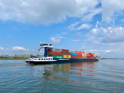Inland barge freight shipping transport sailing pass Dordrecht in Holland in the Netherlands on calm river water of the Maas. Container ship transporting goods in colorful metal containers. Scenic 