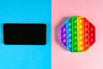 Anti-stress silicone toy popit on pink-blue background with smartphone