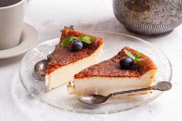 Slice of Homemade Basque burnt cheesecake on a plate with blueberries and mint leaves on light background.